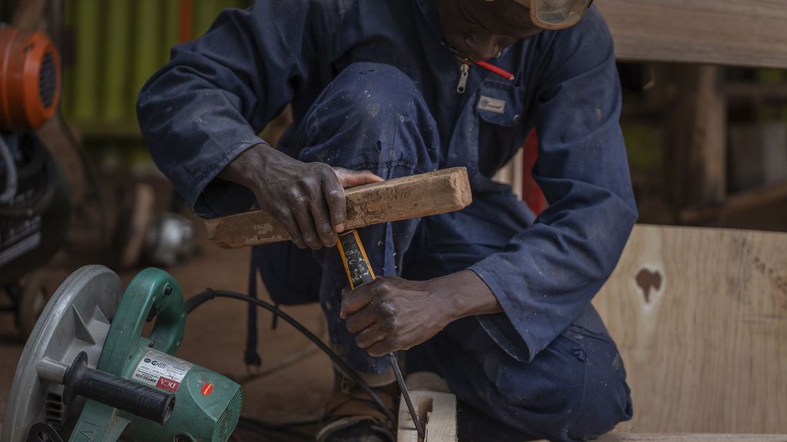 Ezra, 25, ein junger und sehr erfolgreicher Tischler, der Begünstigter von UYDEL ist, lächelt in seiner Werkstatt, während er am 7. Februar 2025 in Kampala, Uganda, das Gestell eines Bettes für einen Kunden baut. Ezra hat für seine Arbeitsleistung einen Wirtschaftspreis gewonnen. Er sagte, er sei stolz auf diese Anerkennung. Er spart Geld, um ein Fahrzeug zu kaufen, mit dem er Möbel für Kunden durch die Stadt transportieren kann. Er möchte einen Ausstellungsraum eröffnen, in dem die Menschen seine Möbelstücke kaufen können. Er sagte, dass die Unterstützung und Ausbildung, die er von UYDEL erhalten hat, für seine Entwicklung zu einem erfolgreichen Tischler von entscheidender Bedeutung war.